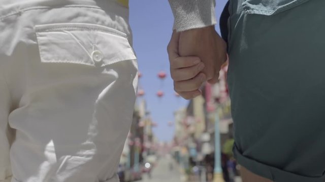Closeup On Hand Holding Multiracial Gay Couple Walking Down The Street In Chinatown, San Francisco
