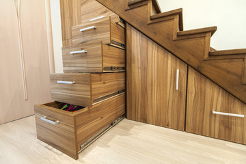 Modernes Architekturinterieur mit Luxusflur mit glänzender Holztreppe im modernen Etagenhaus. Maßgefertigte ausziehbare Schränke auf Gleitern in Schlitzen unter Treppen
