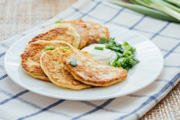 Vegetable fritters with sour cream and chopped leek on white plate 