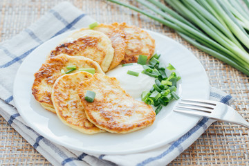 Vegetable fritters with sour cream and chopped leek on white plate 