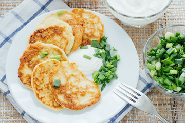 Vegetable fritters with sour cream and chopped leek on white plate 