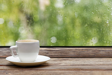 White steaming cup of hot coffee on vintage wooden windowsill or table against window with...