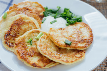 Vegetable fritters with sour cream and chopped leek on white plate 