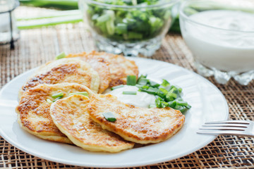 Vegetable fritters with sour cream and chopped leek on white plate