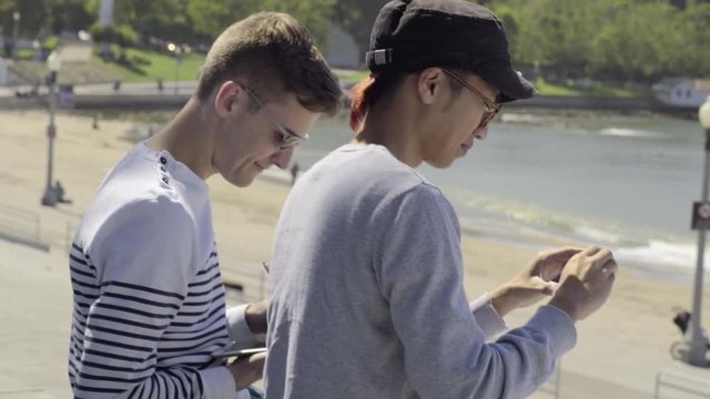 Gay Couple Enjoy Hanging Out At The Beach, Drawing On A Tablet And Taking Photos With Smart Phone 