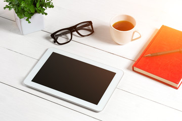 Office table desk with set of supplies, red notepad, cup, pen, tablet, glasses, flower on white background. Top view