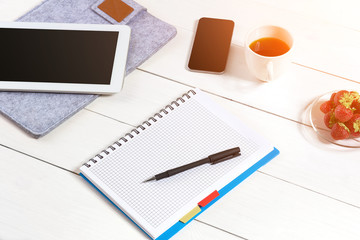 Office table desk with set of supplies, white blank notepad, cup, pen, tablet on white background. Top view