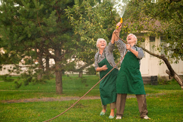 Senior people having fun. Man and woman, water hose. Under the rain.