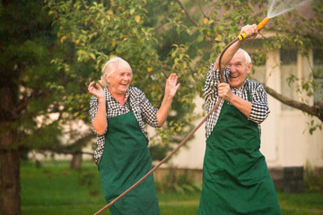 Cheerful people outdoors. Couple with garden hose.