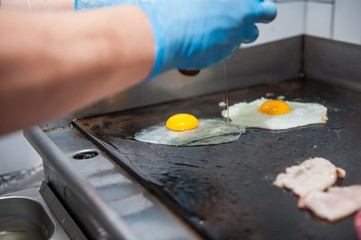 Chief cook preparing fresh burger in the kitchen. Burger restaurant menu cooking process. The chief cooks fried eggs on the grill with cutlets and bacon. Fast food cafe cuisine. Selective focus