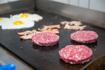 Burger restaurant menu cooking process. Eggs, cutlets and bacon are fried on a grill. Fast food cafe cuisine. Selective focus. close up