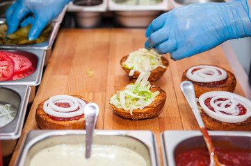 Chief cook preparing fresh burger in the kitchen.Burger restaurant menu cooking process. The cook put ingridients together by layers. Fast food cafe cuisine. Selective focus. close up