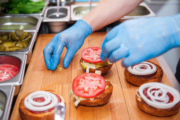 Chief cook preparing fresh burger in the kitchen.Burger restaurant menu cooking process. The cook put ingridients together by layers. Fast food cafe cuisine. Selective focus. close up