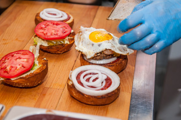 Chief cook preparing fresh burger in the kitchen.Burger restaurant menu cooking process. The cook put ingridients together by layers. Fast food cafe cuisine. Selective focus. close up
