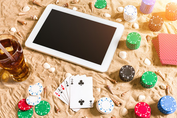 Gambling on vacation concept - white sand with seashells , colored poker chips and cards. Top view