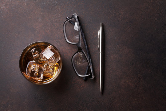 Whiskey with ice, pen and eyeglasses