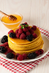 Fresh made delicious pancakes with berries, blackberries, raspberries, banana, honey and maple syrup. Healthy morning breakfast concept.