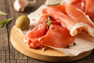 closeup of thin slices of prosciutto with mixed olives and paprika on wooden cutting board