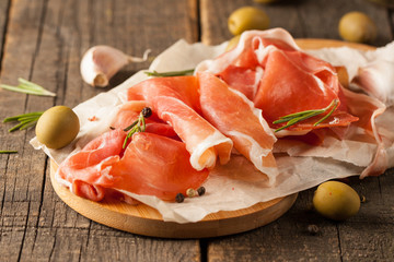 closeup of thin slices of prosciutto with mixed olives and paprika on wooden cutting board