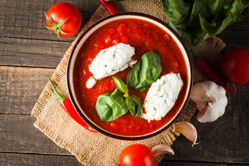 Chili tomato soup with sour cream sauce, cottage cheese, basil and red hot peppers on wooden background. Healthy, vegan and dieting lunch and dinner concept.