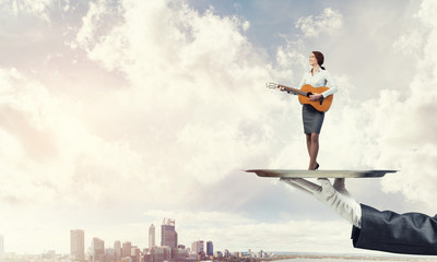 Attractive businesswoman on metal tray playing acoustic guitar against cityscape background