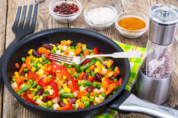 Cooked mixed vegetables in frying pan on wooden table