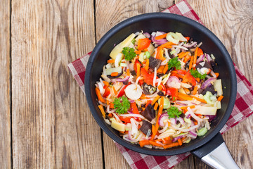 Frozen cooked vegetable mix in frying pan on wooden background, 
