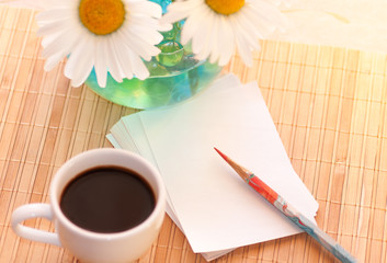 Coffee black, paper and a red pencil on the background of a vase with chamomiles