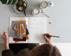 Overhead view of female fashion designer sketching in book