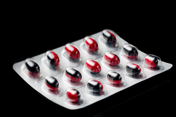 Red and black color capsules pills in blister pack on black background