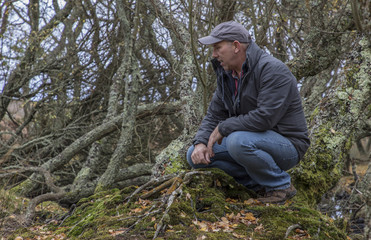 man in copse crouching looking at scenery