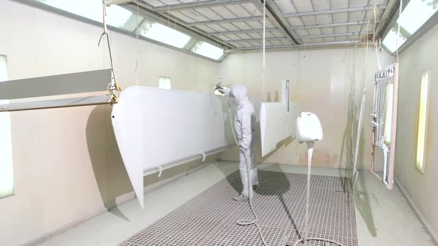 Worker spray painting plane wing. Person wearing mask and coveralls. Chemical resistant workwear.