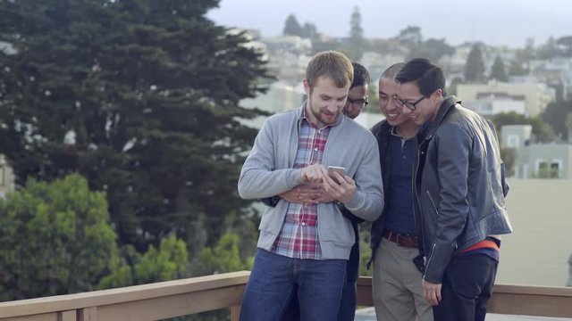 Group Of Gay Men Look Through Their Friend's Smart Phone Pics At A Party In San Francisco 