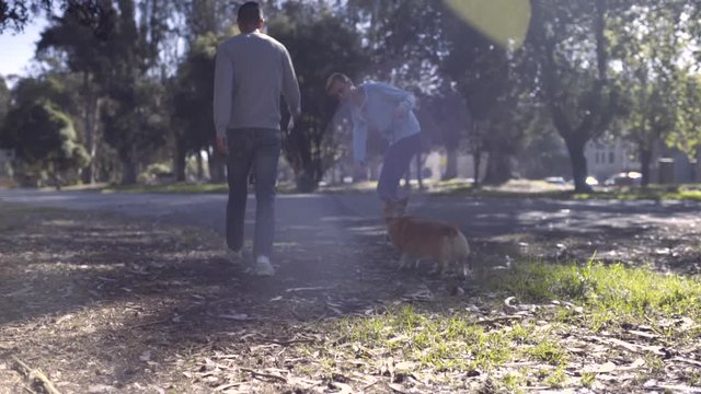 Gay Couple Take Corgi Dog For A Walk In Park, Owner Shakes Bag Of Treats For Dog