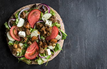 Opened tortilla wrap sandwich with ground meat and vegetables salad on dark background with blank space