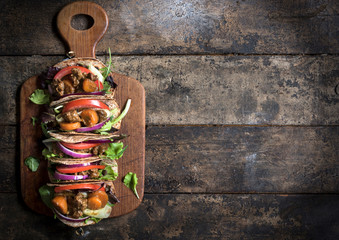 Mini tortilla sandwiches with ground meat and vegetables salad on wooden background with blank space