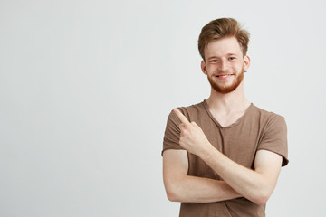 Portrait of young handsome sincere man with beard smiling looking at camera pointing finger in side...