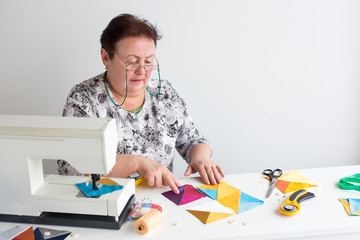 needlework and quilting in the workshop of a tailor woman - elderly women tailor put on the desktop pieces of colored fabric, lay next to the scissors, buttons, pins and thread for sewing machine