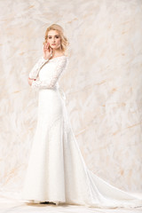 Fototapeta na wymiar fashionable white gown, beautiful blonde model, bride hairstyle and makeup concept - young charming lady in wedding festive dress with train standing indoors on light background, pretty woman posing