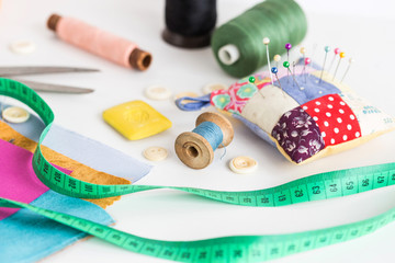 tailoring and fashion concept, patchwork, closeup sewing tools - working environment on a white table, thread spools, buttons, meter, pincushion, scissors, pieces of colored patchwork fabric, soap