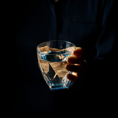 female hand isolated on black showing glass of water