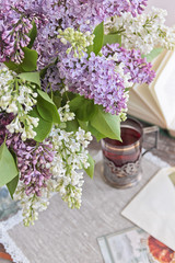 A bouquet of lilacs, a cup of tea, a book and a postcard on a wooden background