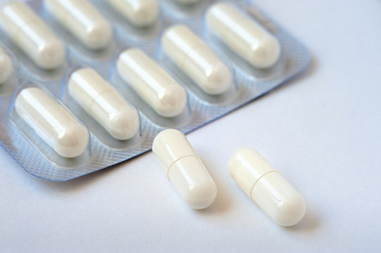 Two white pills lie on a white table. Packing tablets in the background. Concept of health, medicine, pharmacology