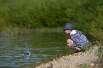 A boy sits and throws stones into the water