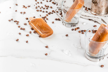 Summer desserts. Frozen drinks. Sweet popsicles made from coffee and milk. In coffee cups, On a white marble table, with coffee beans. Copy space