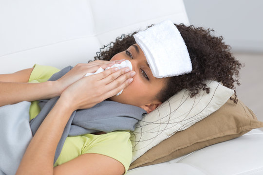 sick woman blowing her nose on sofa at home
