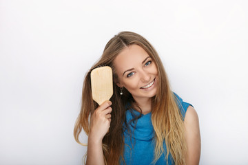 Fototapeta premium Headshot of young adorable blonde woman with cute smile with comb in hand brush her hair on white background