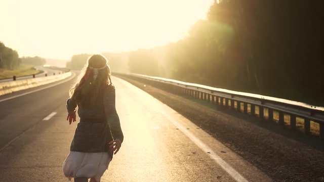 girl in the hippie clothes runs on the road at dawn. girl is on the road at dawn. young attractive woman in hippie clothes smiling and looking at camera. slow motion