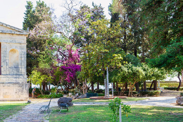 Beautiful green park on Corfu island in Greece. Bench, decorations and a man working on background.