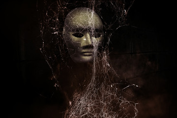 Mysterious woman in black wearing white mask hidden behind spider web,Scary background for book...